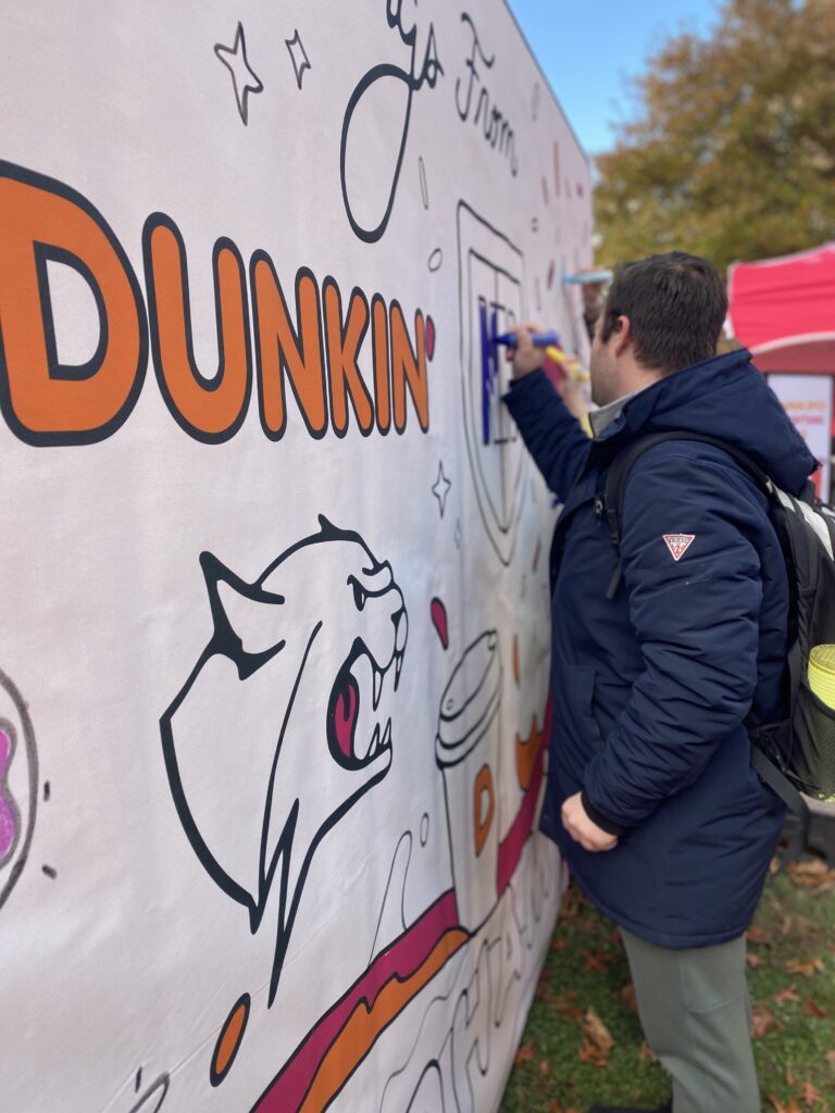 Students at UNH Durham fill in a freestanding mural created by Rachel Sotak in collaboration with Dunkin' Donuts.