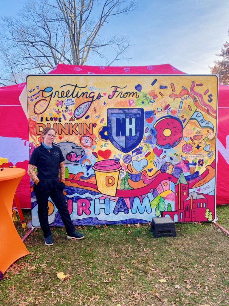Rachel Sotak poses in from of an interactive mural experience she designed for students at UNH, in conjunction with Dunkin' Donutes